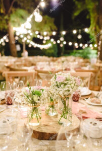 Flowers decorating the centerpieces with luxury cutlery on the tables of a wedding hall.